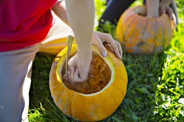 High angle view of brother and sister removing pumpkin pulp on field - CAVF48176