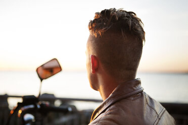 Rear view of motorcyclist looking at sea view during sunset - CAVF48204