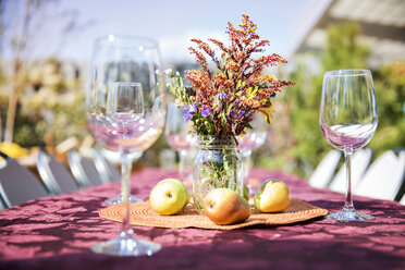 Leere Weingläser mit Obst und Blumenvase auf einem Tisch im Freien bei einer Gartenparty - CAVF48218