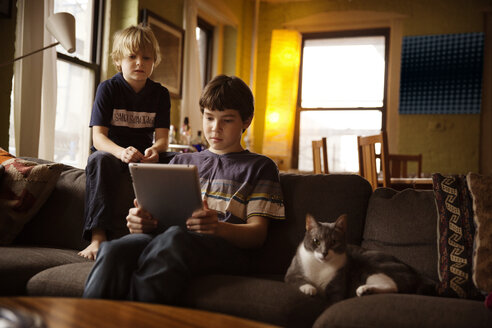 Junge benutzt Tablet-Computer, während er neben seiner Katze auf dem Sofa sitzt - CAVF48265