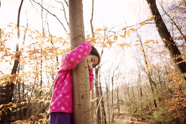 Portrait of girl embracing tree trunk at yard during autumn - CAVF48296