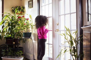 Side view of girl looking through glass door at home - CAVF48299