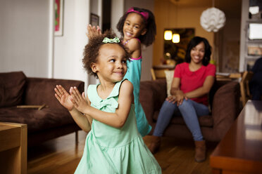 Mutter schaut auf glückliche Töchter, die im Wohnzimmer tanzen - CAVF48344