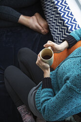 Blick von oben auf eine Frau mit Kaffeetasse, die auf einem Nischenfensterplatz sitzt - CAVF48357