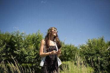 Happy woman wearing tiara standing on field against blue sky - CAVF48435