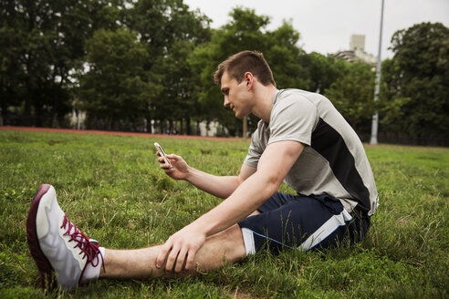 Mann benutzt Smartphone, während er auf einem Feld im Park sitzt - CAVF48452