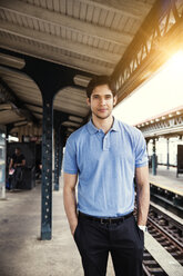 Portrait of man with hands in pockets standing at railroad platform - CAVF48466