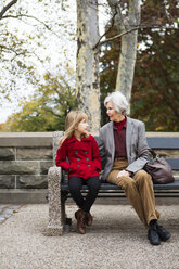 Woman looking at granddaughter while sitting on bench at park - CAVF48559