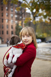 Portrait of smiling girl carrying dog while standing on footpath - CAVF48586