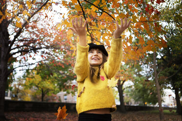 Happy girl playing with maple leaves in park during autumn - CAVF48589