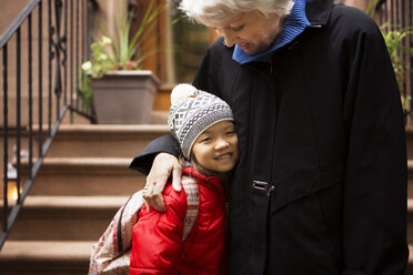 Mädchen lächelt, während sie mit ihrer Großmutter auf einer Treppe steht - CAVF48615