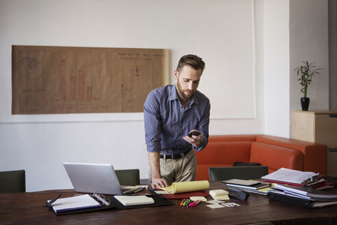 Mann benutzt Smartphone bei der Arbeit im Büro - CAVF48647