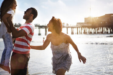 Woman looking at man carrying daughter while enjoying at beach - CAVF48661