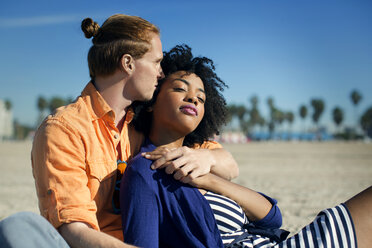 Affectionate couple relaxing on sand against sky - CAVF48688