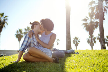 Zärtliches Paar, das sich küsst, während es auf einem Feld vor dem Himmel sitzt - CAVF48695