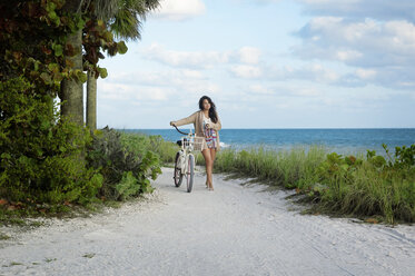 Frau mit Fahrrad zu Fuß auf Sand gegen das Meer - CAVF48729
