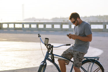 Mann benutzt sein Smartphone, während er auf dem Fahrrad sitzt - CAVF48731