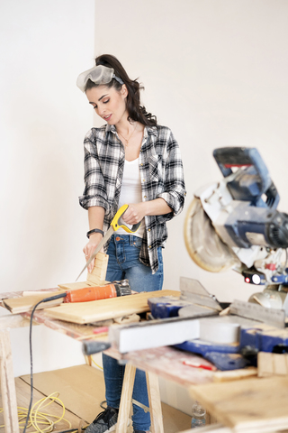 Junge Frau renoviert ihre neue Wohnung, sägt ein Stück Holz, lizenzfreies Stockfoto