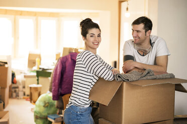 Happy couple moving house, standing by cardboard box - PESF01058