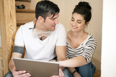 Young couple refurbishing new home, sitting on stairs using digital tablet - PESF01060