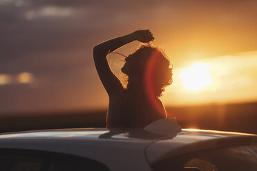 Frau außerhalb des Autos bei Sonnenuntergang, erhobener Arm - JPF00304