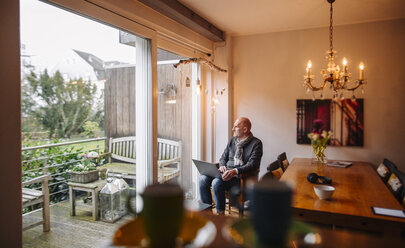 Senior man sitting at home, using laptop - GUSF00672