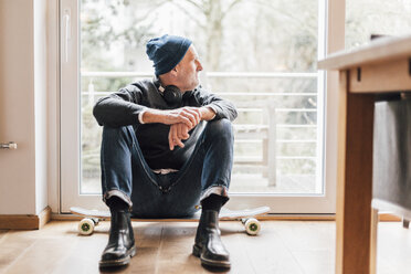 Cooler älterer Mann, der auf dem Boden sitzt und aus dem Fenster schaut - GUSF00673