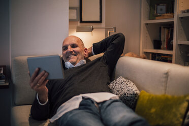 Senior man lying on couch, reading e-book - GUSF00675