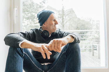 Cool senior man sitting on longboard, looking out of window - GUSF00697