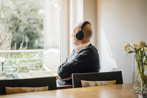 Älterer Mann sitzt zu Hause, hört Musik und schaut aus dem Fenster - GUSF00699