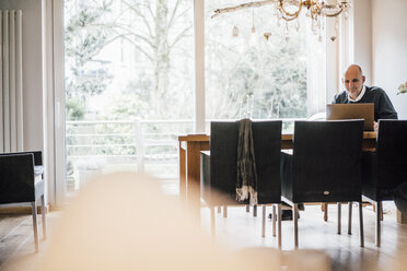 Senior man sitting at home, using laptop - GUSF00700