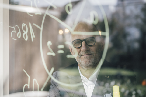 senior Businessman beim Brainstorming, Formeln auf Fensterscheibe zeichnen, lizenzfreies Stockfoto