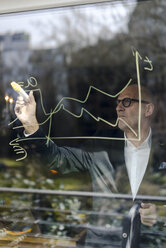 senior businessman brainstorming, drawing formulas on window pane - GUSF00710