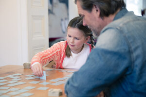 Vater und Tochter spielen Memory auf einem Tisch zu Hause - MOEF01078