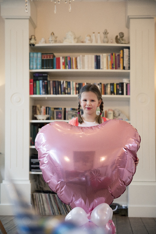 Porträt eines Mädchens mit Zöpfen, das einen großen herzförmigen Luftballon hält, lizenzfreies Stockfoto