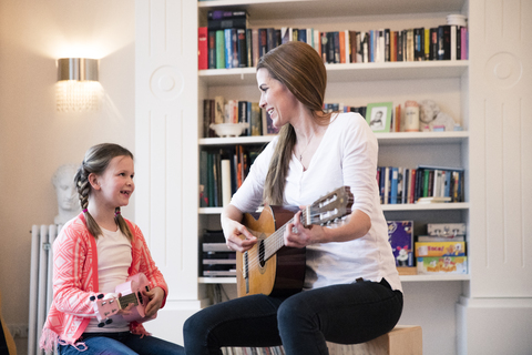 Mother and daughter playing guitar together at home stock photo