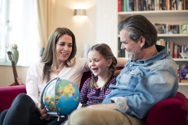 Glückliche Familie auf der Couch sitzend mit Globus - MOEF01107