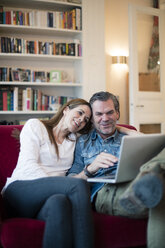 Happy couple sitting on couch using laptop - MOEF01108