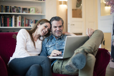 Happy couple sitting on couch using laptop - MOEF01109