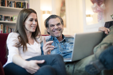 Happy couple sitting on couch using laptop - MOEF01110