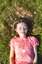 Porträt eines lächelnden Mädchens, das im Frühling im Gras liegt und Gänseblümchen im Haar hat - SARF03679