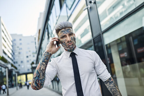 Junger Geschäftsmann mit tätowiertem Gesicht, der am Telefon spricht - ZEDF01332