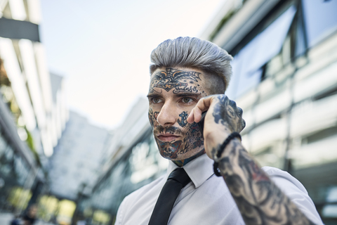 Junger Geschäftsmann mit tätowiertem Gesicht, der am Telefon spricht, lizenzfreies Stockfoto