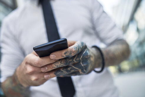 Junger Geschäftsmann mit tätowiertem Gesicht, der ein Smartphone benutzt - ZEDF01339