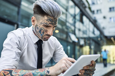 Young businessman with tattooed face, using digital tablet - ZEDF01344