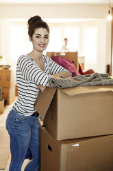 Young woman moving house, unpacking cardboard boxes - PESF01087