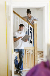Junges Paar steht auf einer Treppe, benutzt ein digitales Tablet und renoviert sein Haus - PESF01091
