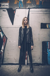 Portrait of serious young woman dressed in black standing in front of graffiti - GUSF00716