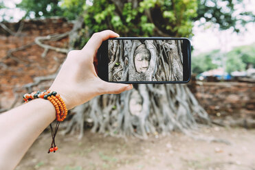 Thailand, Ayutthaya, Wat Mahathat, Frau fotografiert mit Smartphone den Kopf eines Buddhas in den Baumwurzeln - GEMF01913