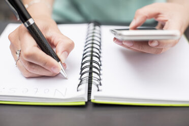 Woman writing notes in diary, holding smartphone - ZEF15378